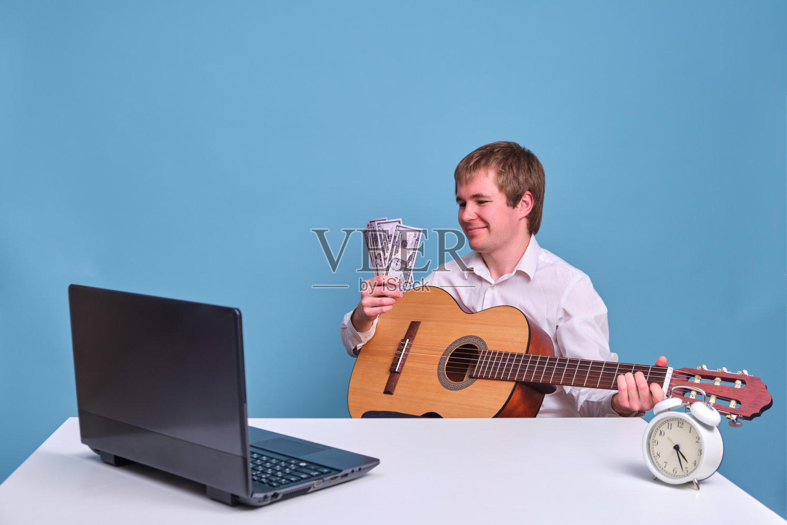 音乐老师坐在电脑前，带着蓝色背景的钱，远程音乐课程和美元工资照片摄影图片