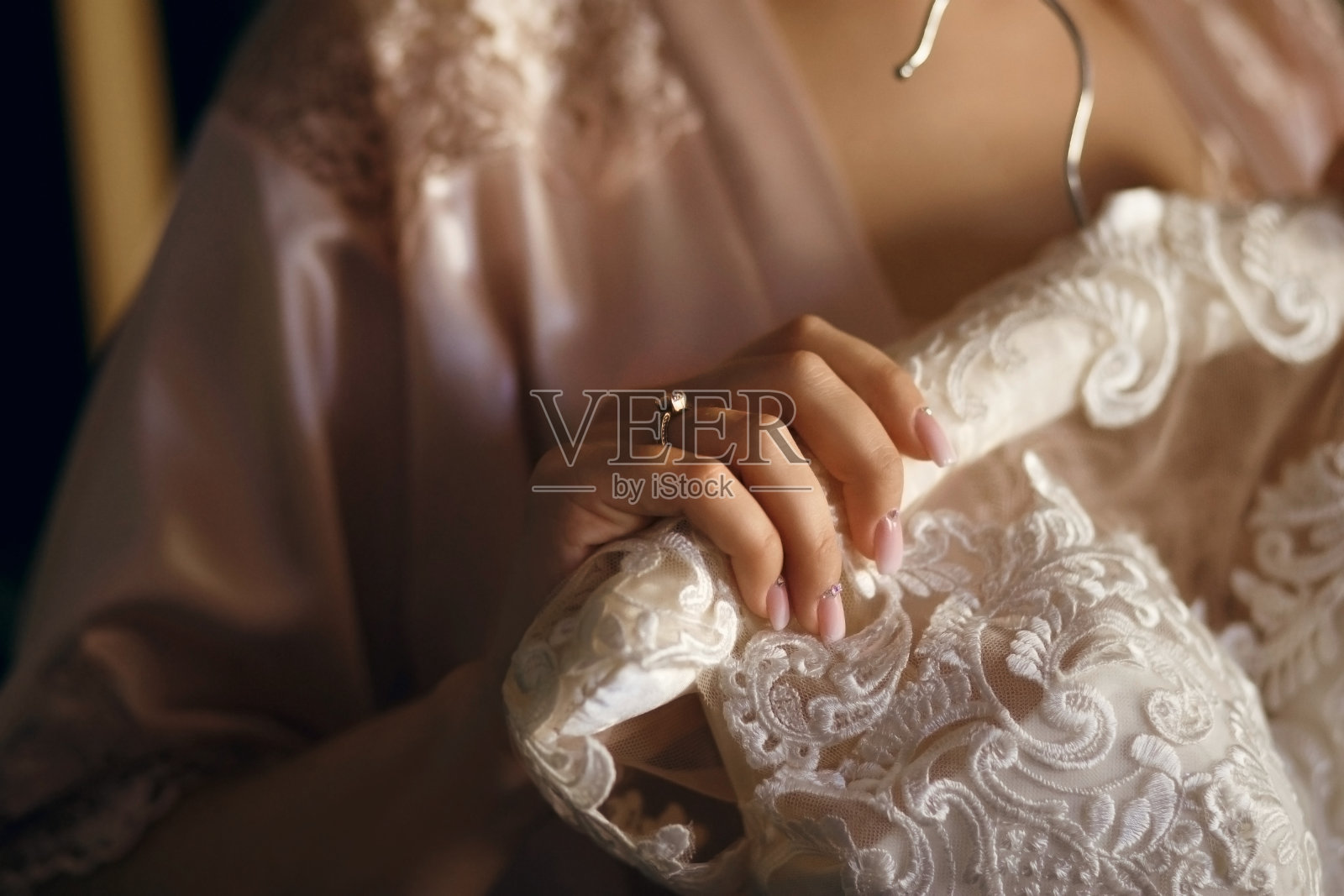 新娘手里拿着一件白色礼服，手指上戴着婚戒，礼服挂在衣架上照片摄影图片
