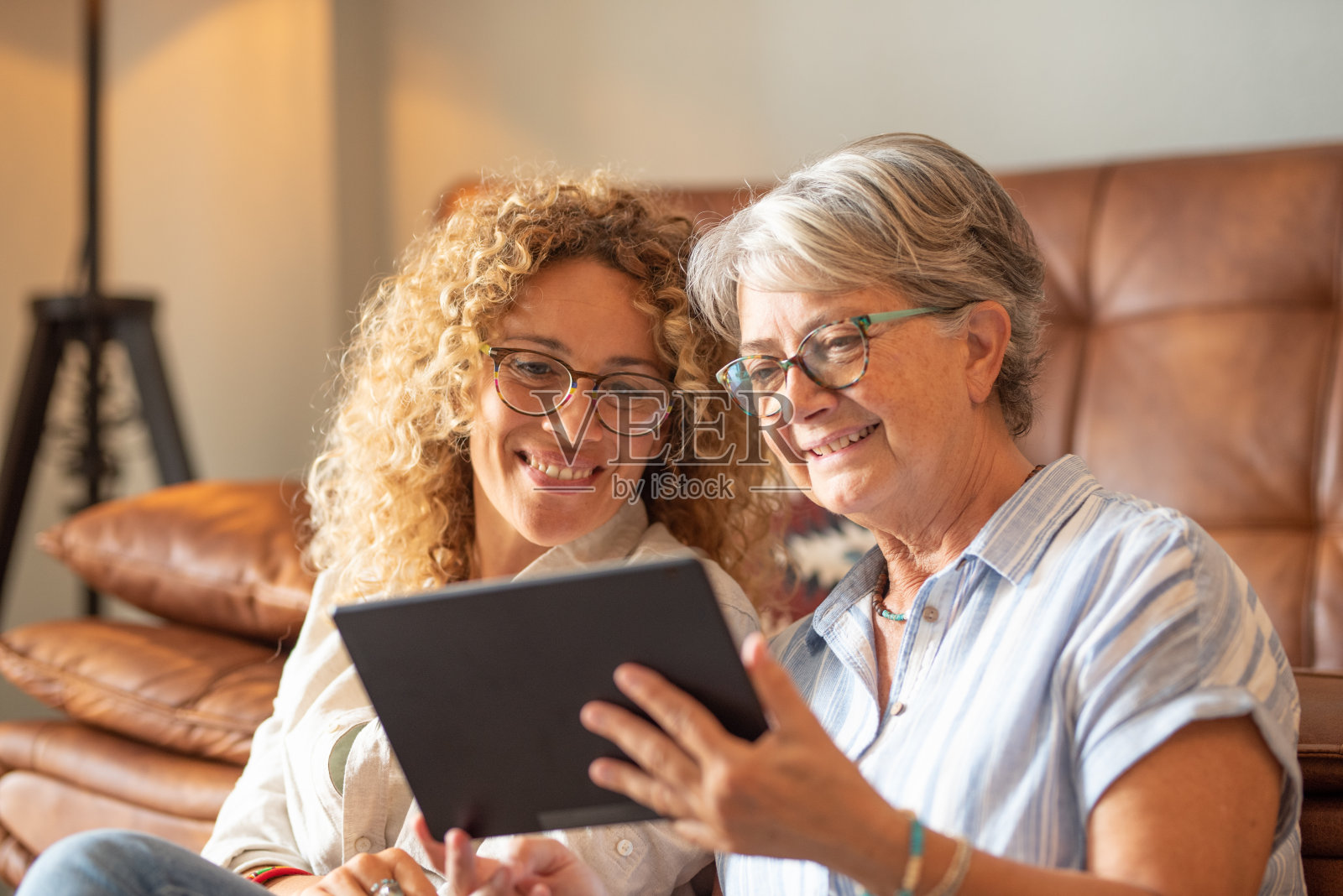 成年美丽的女儿和年迈的母亲坐在家里看数字平板电脑上的社交媒体照片摄影图片