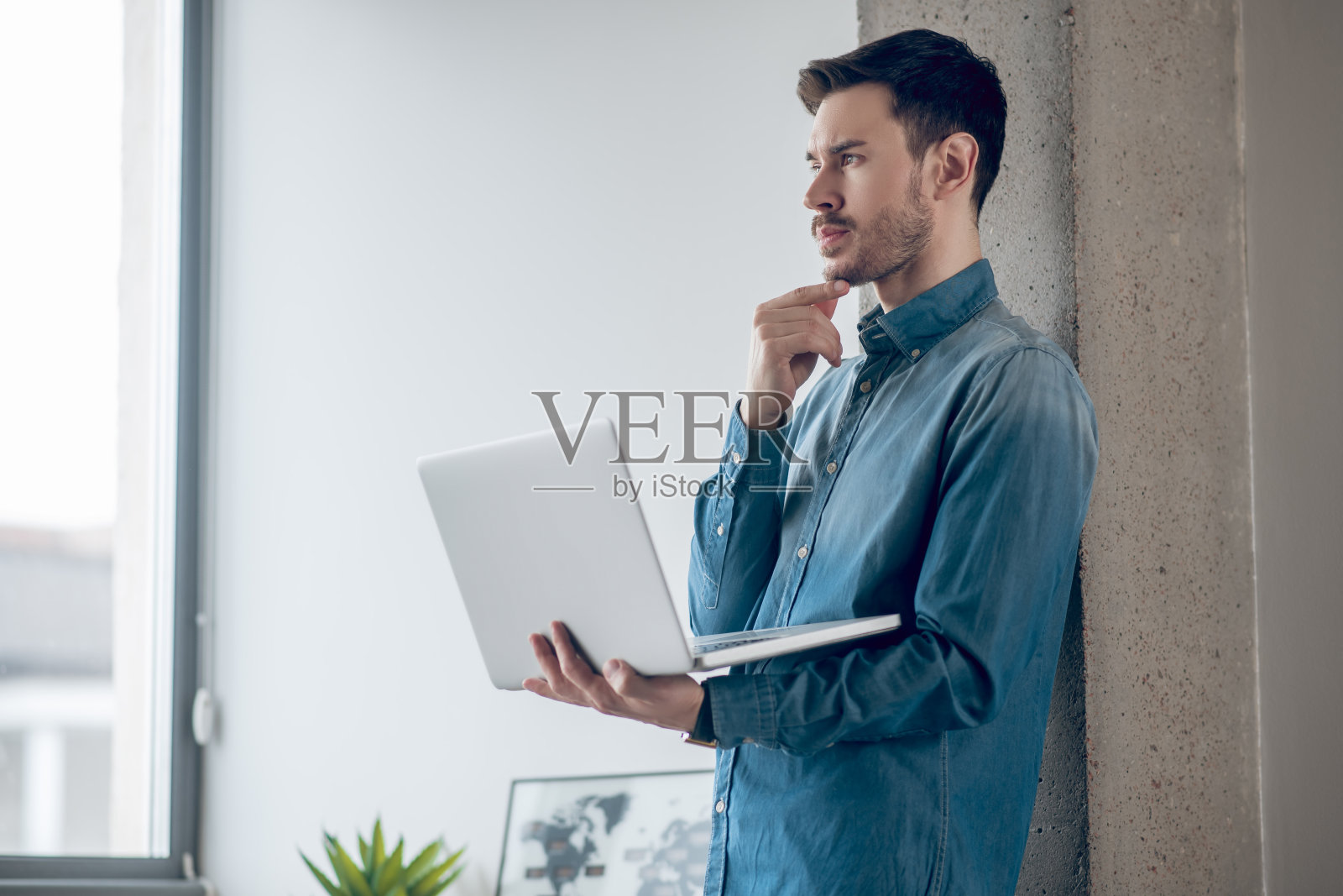 黑头发男子站在窗边，用笔记本电脑工作照片摄影图片