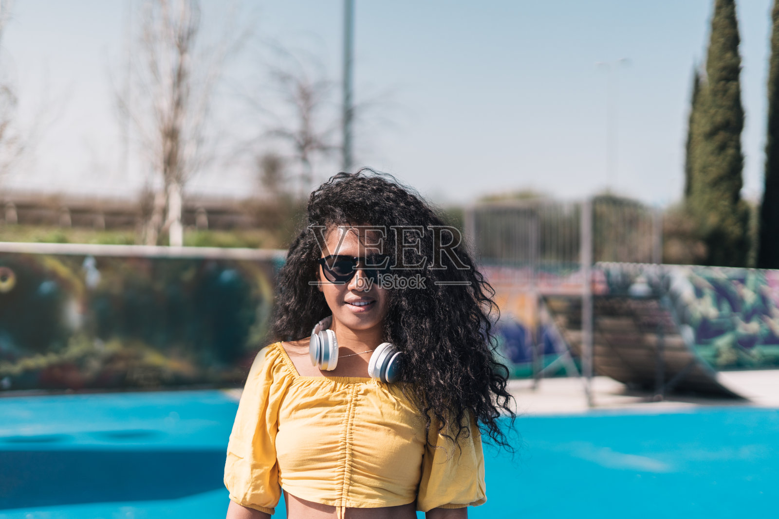 这是一个年轻的非洲裔美国女孩的肖像，她穿着黄色t恤，戴着墨镜，脖子上挂着耳机。照片摄影图片