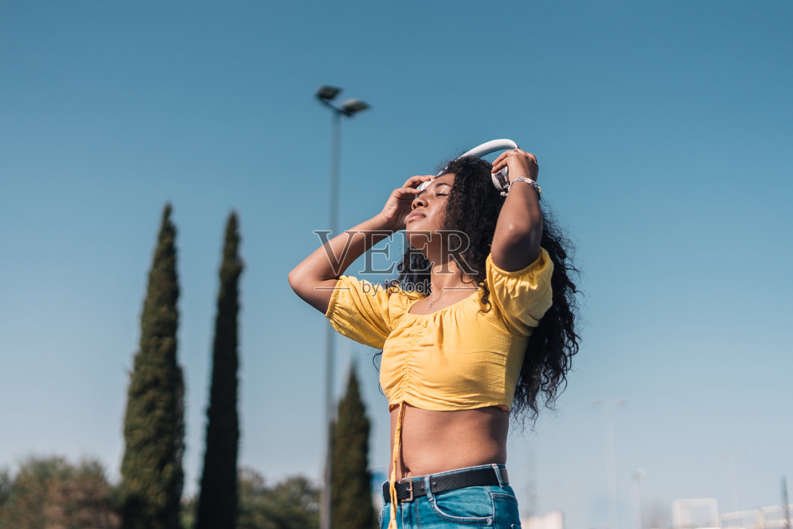 年轻的非洲裔美国女孩微笑着，穿着黄色的t恤，长长的卷发，戴着耳机。照片摄影图片