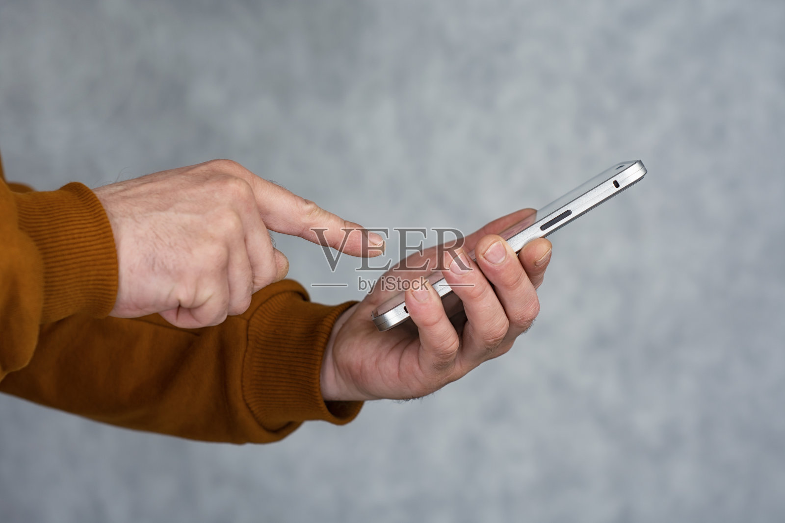 一名身穿棕色夹克的男子手里拿着一部智能手机，用手指按压。照片摄影图片