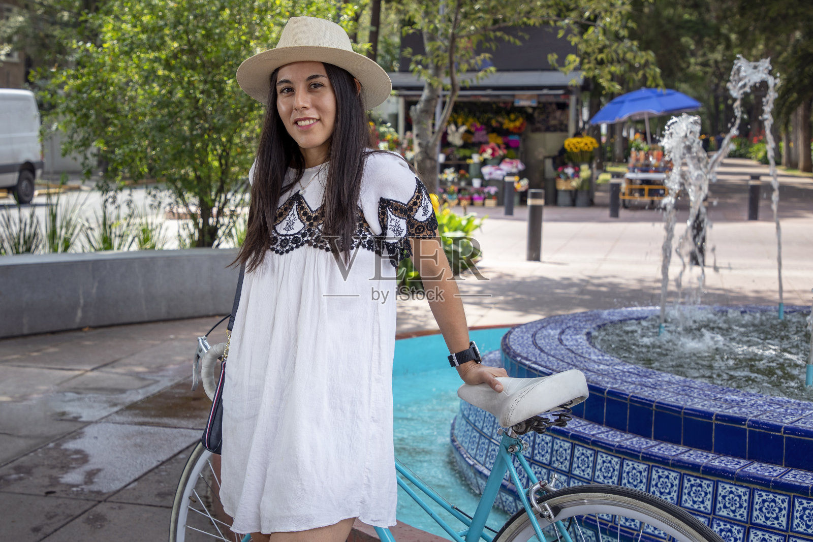在墨西哥城的一天，穿着裙子的拉丁妇女站在喷泉前和她的自行车照片摄影图片