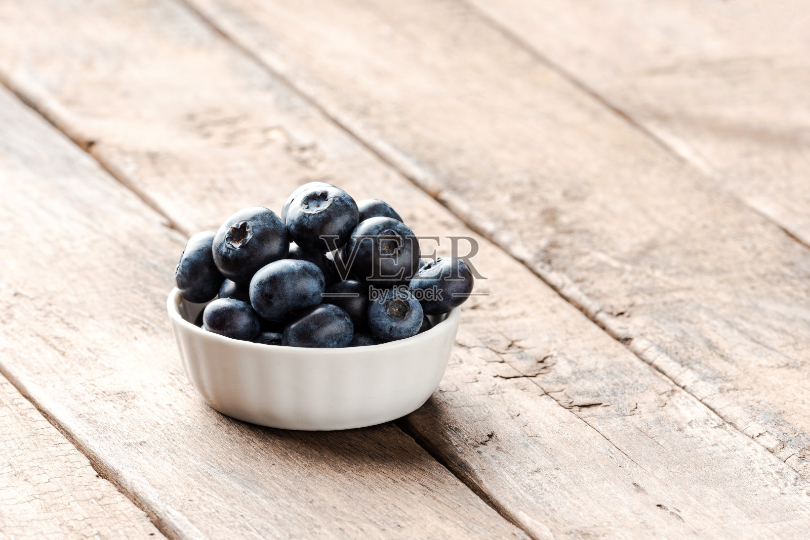 新鲜的蓝莓装在小碗里放在木桌上。近距离照片摄影图片