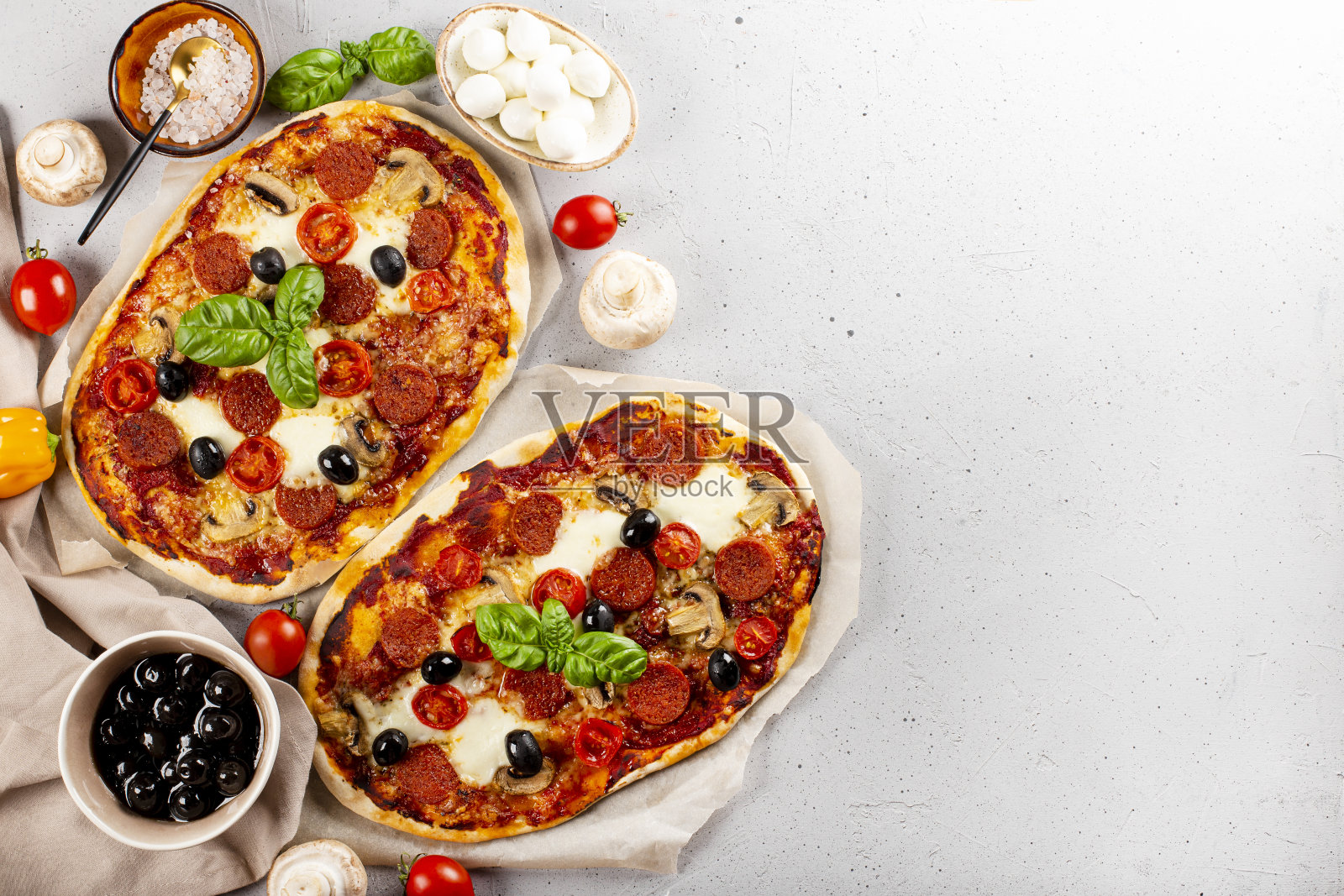 两个新鲜又热的自制意大利披萨，上面有马苏里拉奶酪、意大利辣香肠、橄榄和罗勒，颜色为浅灰色背景照片摄影图片