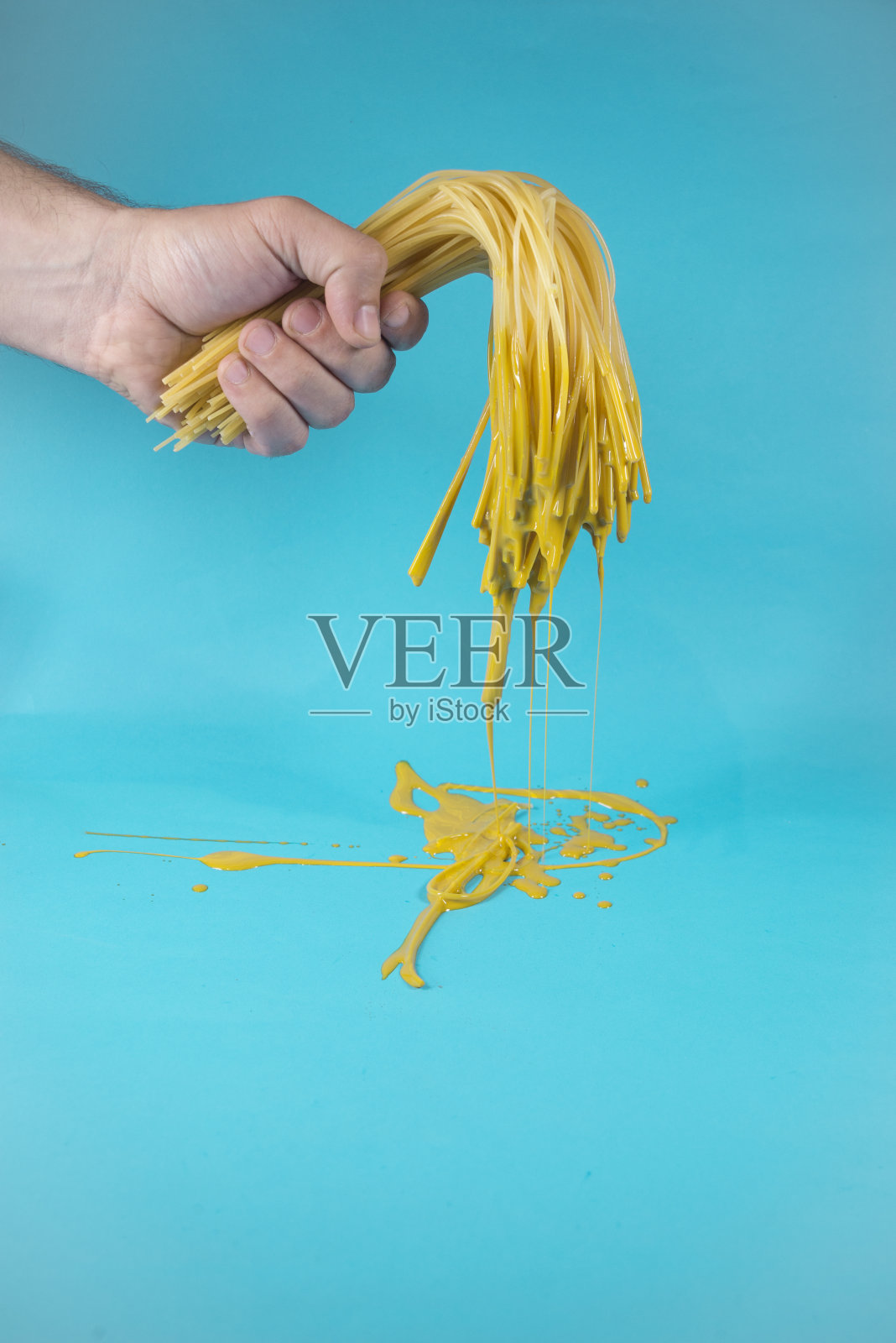 手拿着半熟的意大利面，上面滴着黄色的油漆照片摄影图片