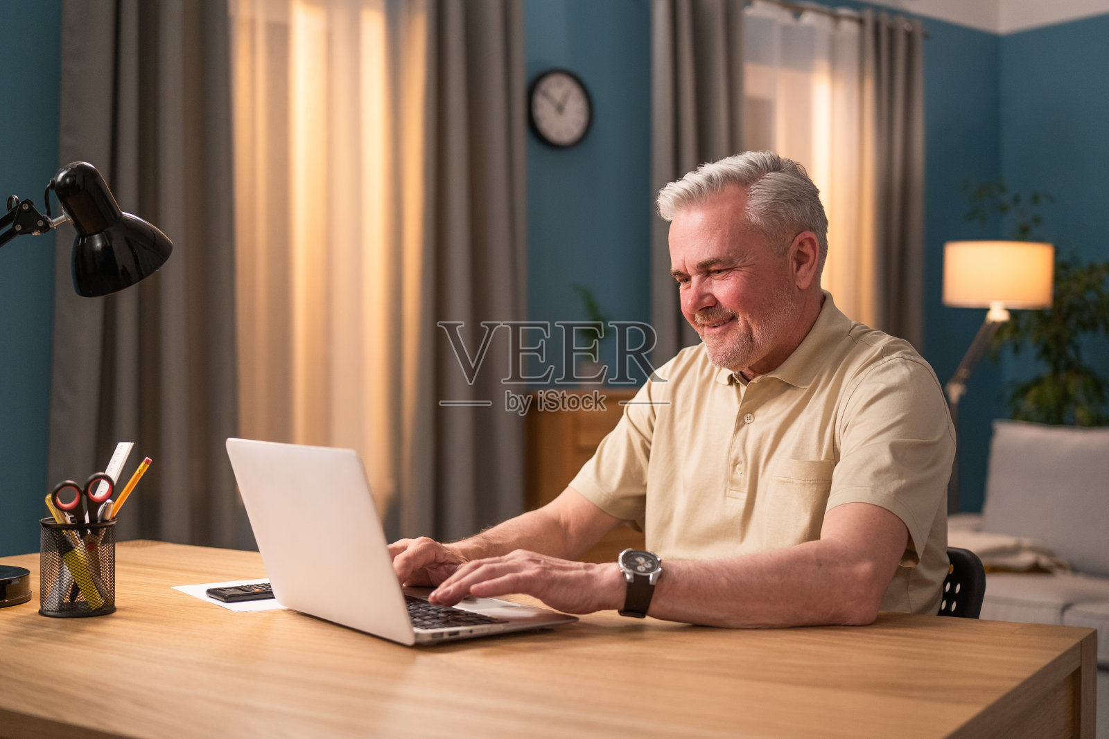 晚上坐在办公桌前用笔记本电脑的老人。Senior在沙龙工作。幸运的退休人员在家里使用电脑。爷爷在网上和孙子聊天。一个面带微笑的大四学生通过他的笔记本电脑的摄像头交谈。一位老人在聊天照片摄影图片