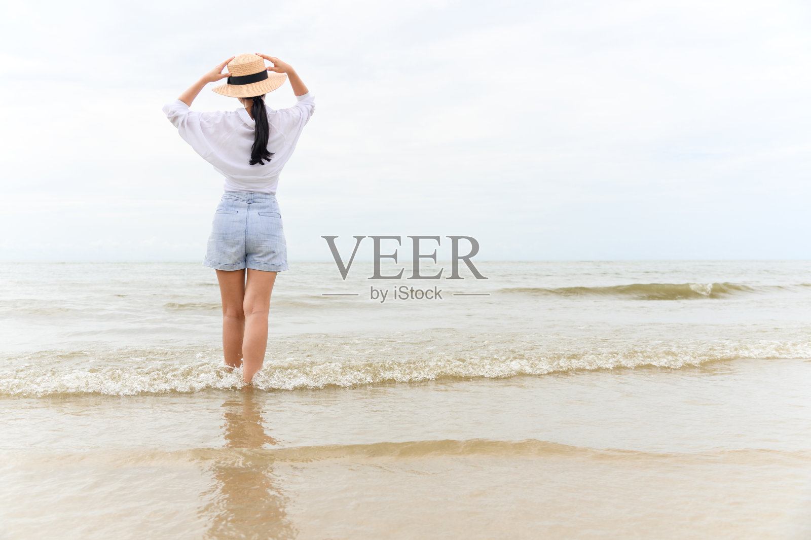 户外夏日写真的年轻亚洲女子戴着草帽望着热带海滩上的大海，享受自由时光、新鲜空气和休闲旅游度假。照片摄影图片