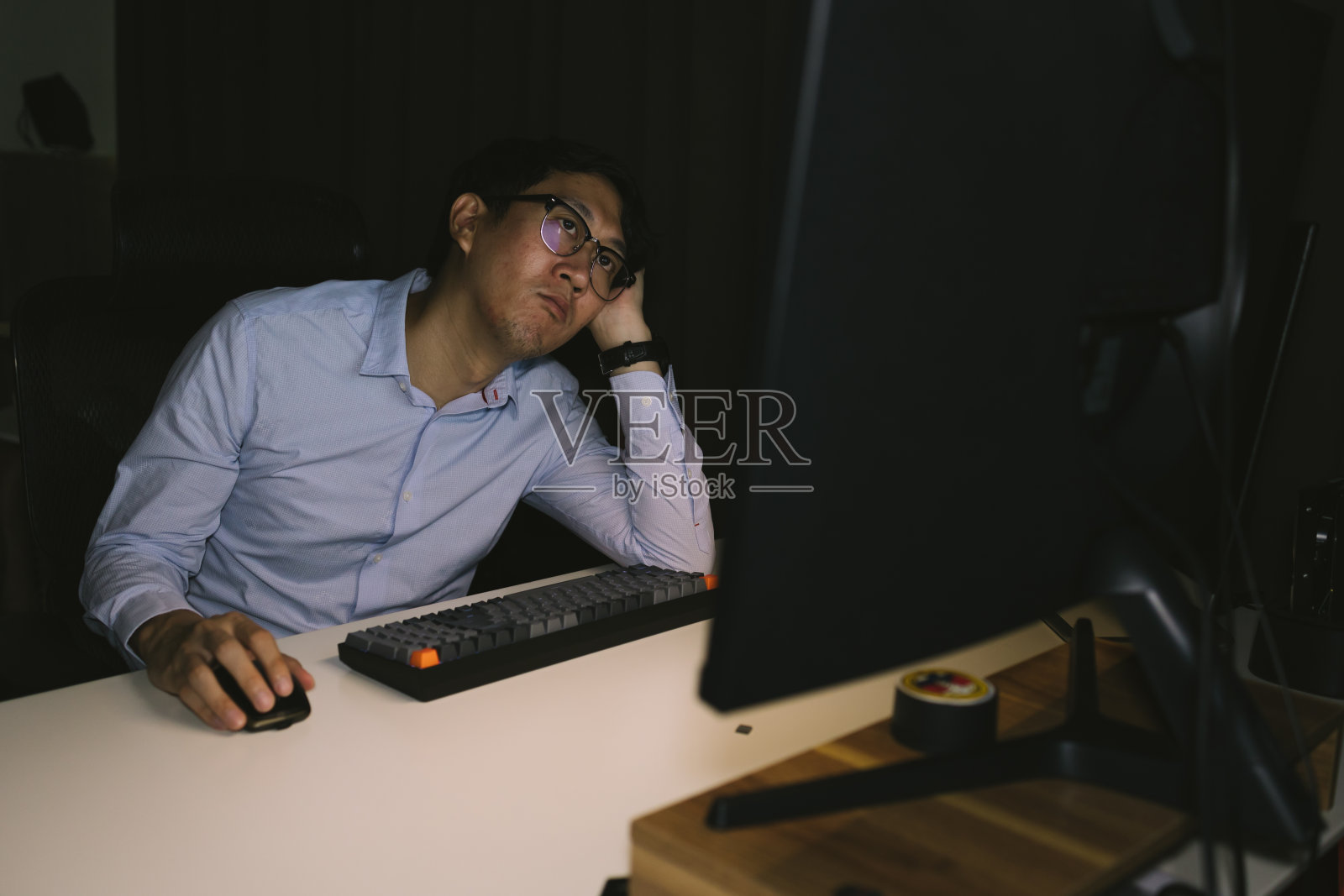 年轻的商人在公司办公室超负荷工作。男性办公室职员在晚上加班时思考和压力照片摄影图片