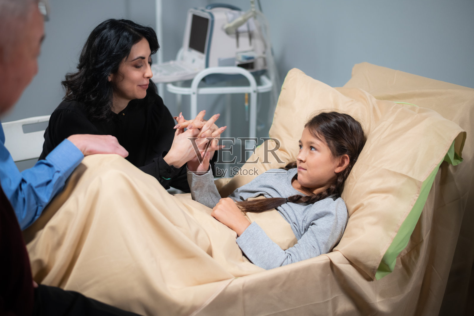 在医院的病房里，一个小女孩和她的家人聊天，他们在给她讲有趣的故事，让她高兴起来，向她表达他们的爱，小女孩微笑着照片摄影图片