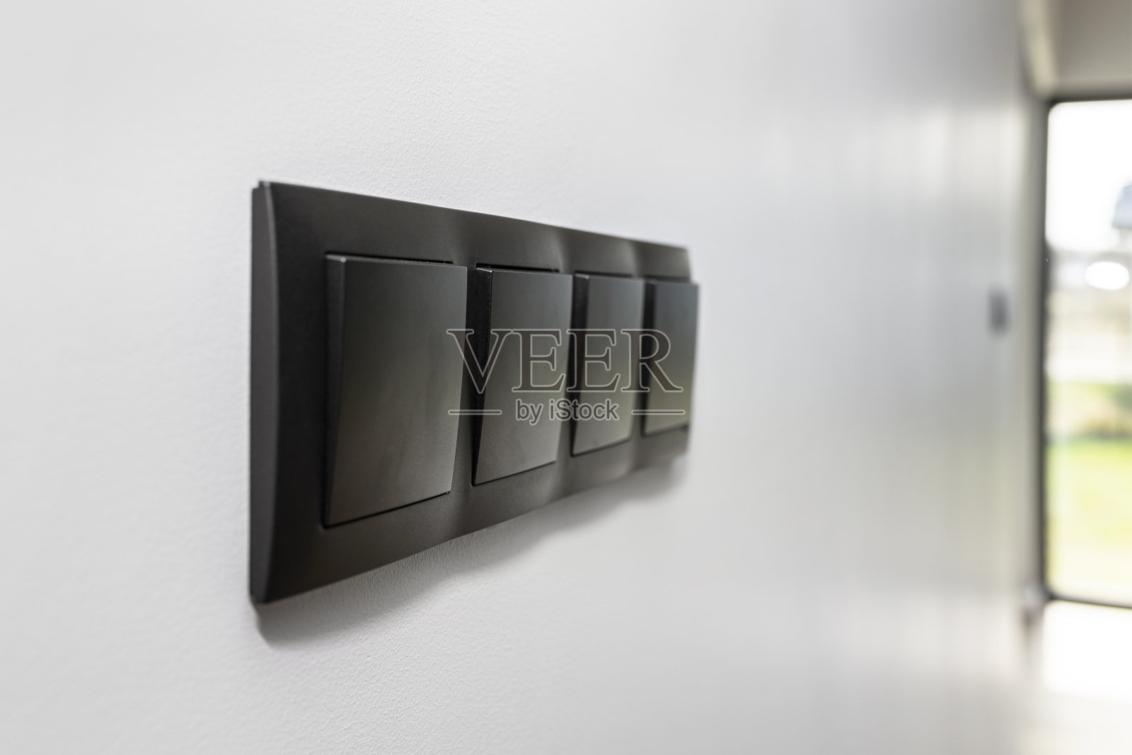 灰色的墙壁上有一个黑色的框架和一个四个按钮的电灯开关。照片摄影图片