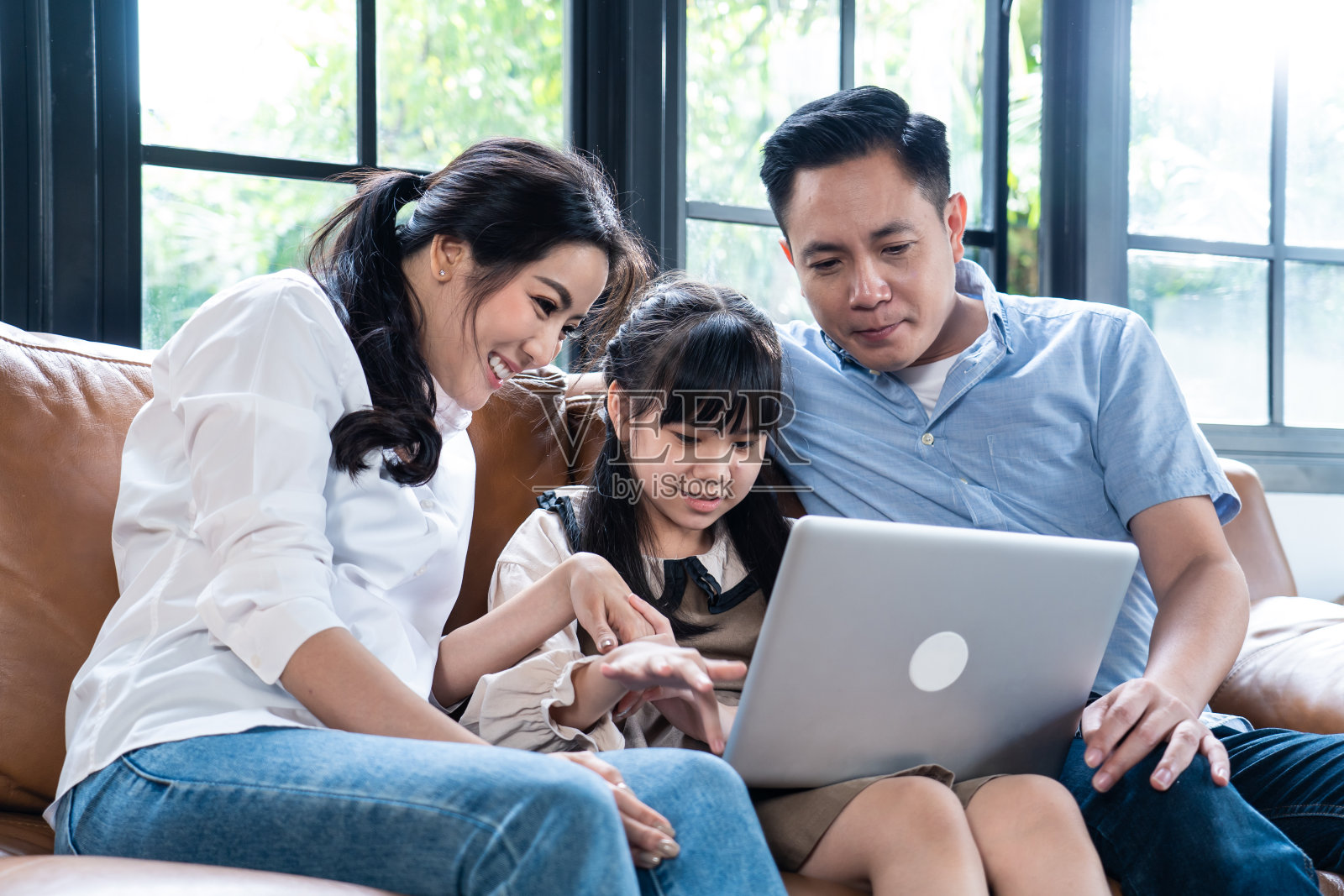 亚洲幸福家庭，年轻的小女孩和父母花时间在一起使用笔记本电脑玩上网在家里的客厅。父亲和母亲通过视频虚拟学习教女儿。照片摄影图片