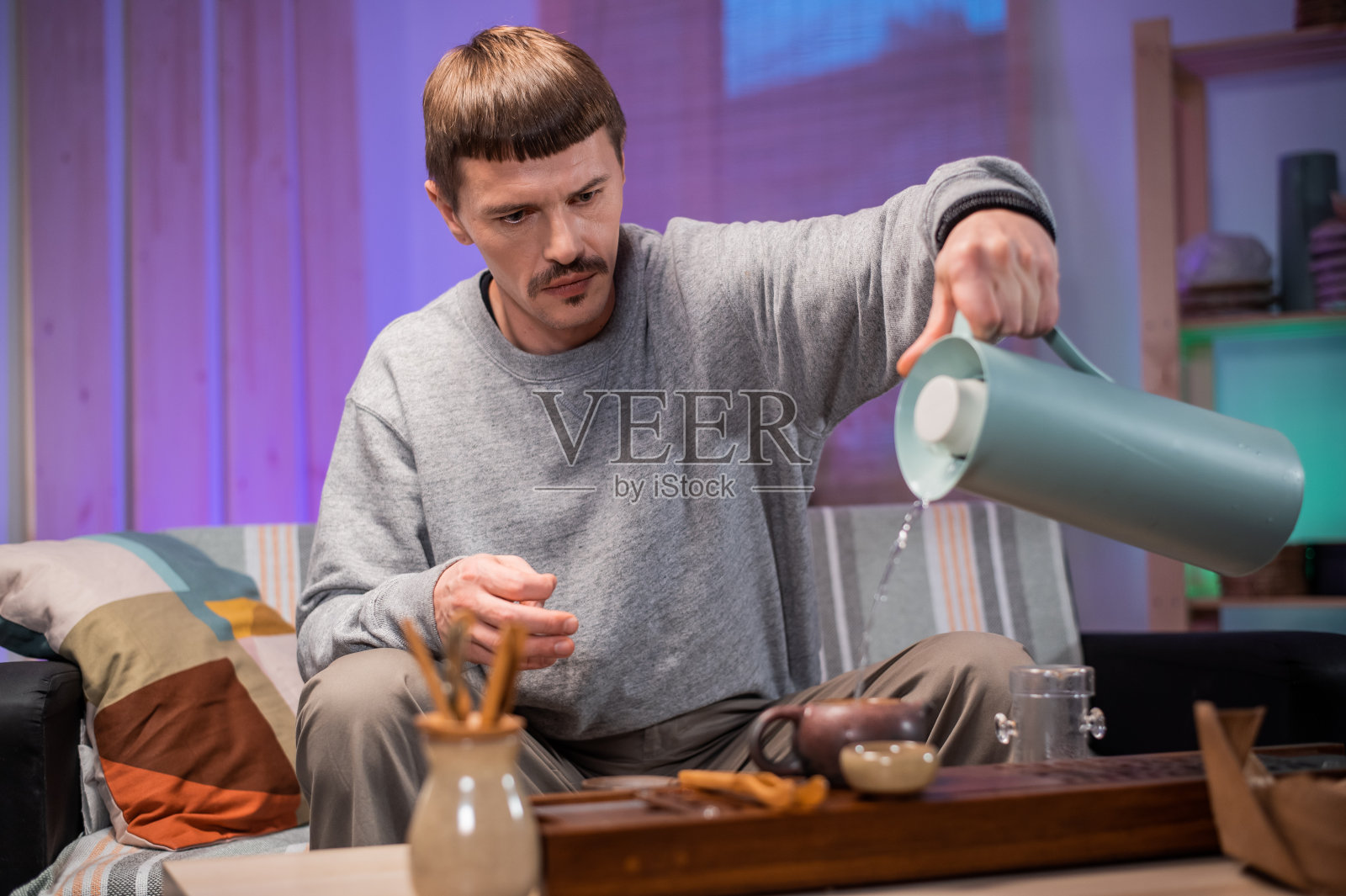 一个男人在家里举行茶道，观察中国茶艺大师的所有传统。将热水从水壶中倒入一个特制的砂茶壶中照片摄影图片
