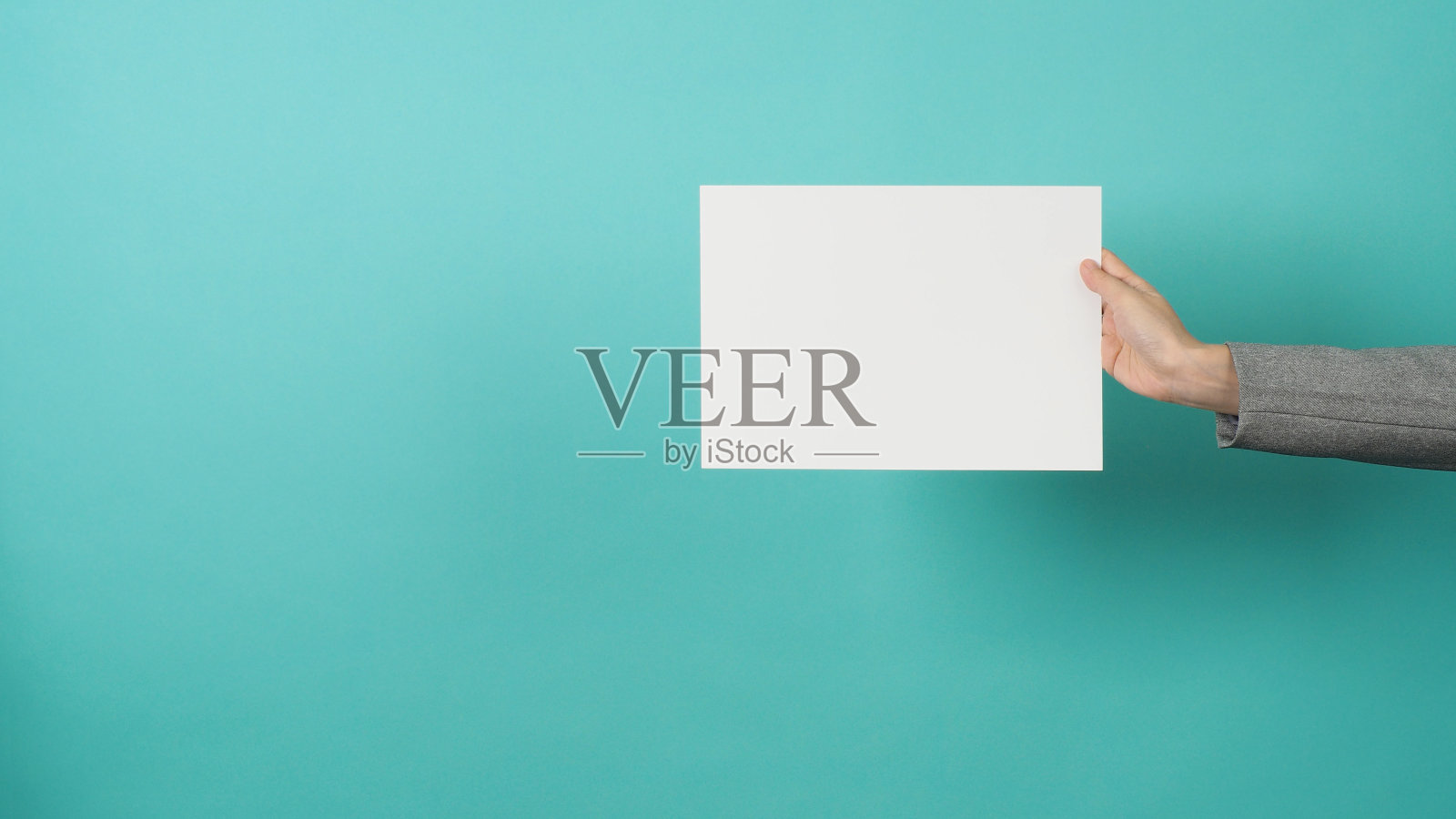 女人手握空白纸，身穿灰色套装孤立在绿色或蒂芙尼蓝色背景照片摄影图片