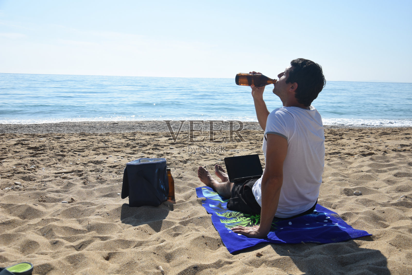 男人喝着啤酒，在海滩上用笔记本电脑工作照片摄影图片