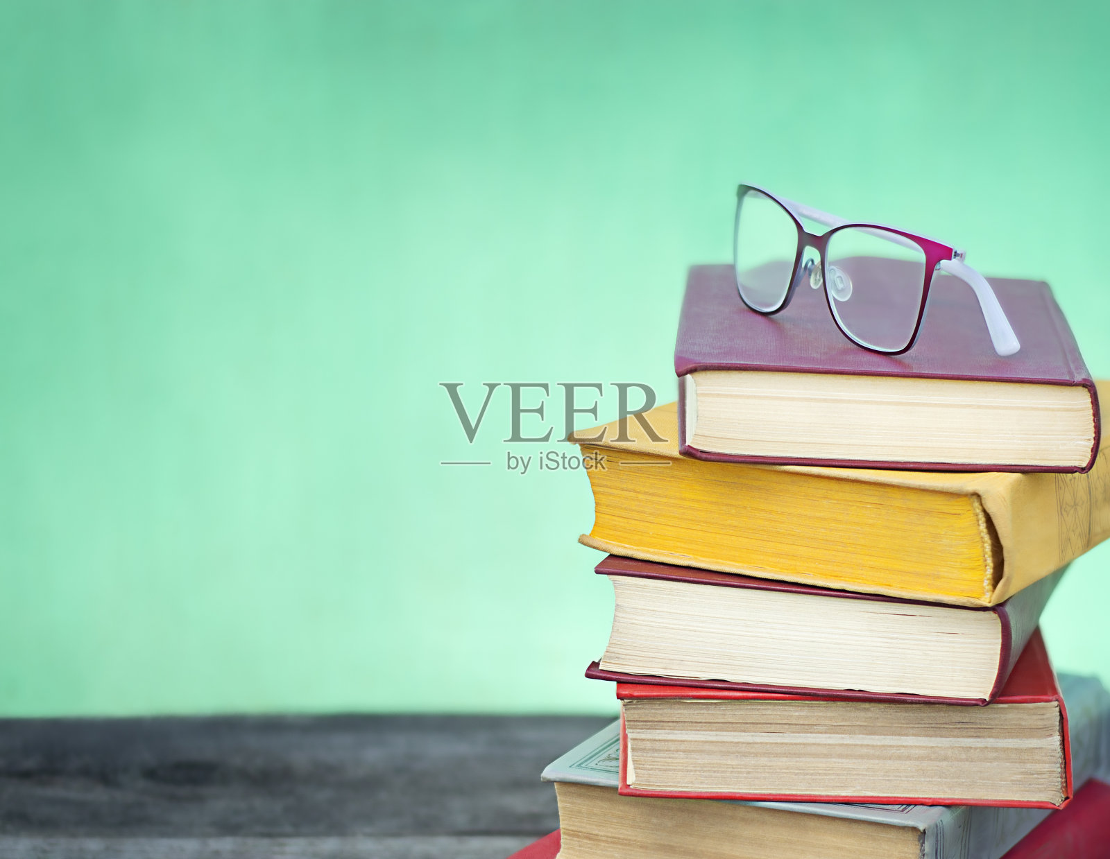 在绿色和蓝色的背景上，堆叠彩色的书和眼镜照片摄影图片