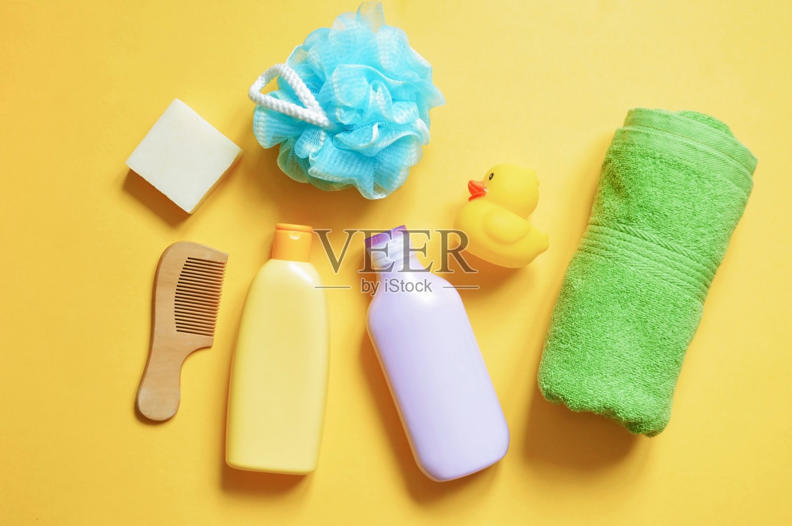 婴儿护理沐浴产品上的黄色背景。香波、沐浴露、绿色卷巾、棉絮、肥皂、橡皮鸭照片摄影图片