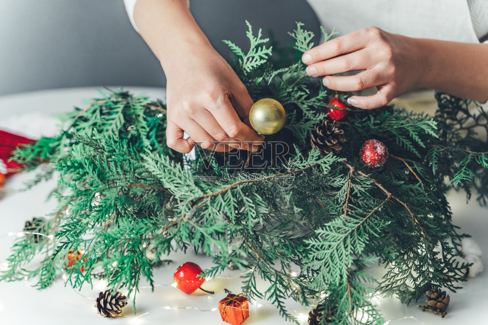 卖花的女人用木盒里的云杉树枝做圣诞装饰品。使用花泡沫，球果，雪苹果，球，棉花花，花环。新年的庆祝活动照片摄影图片