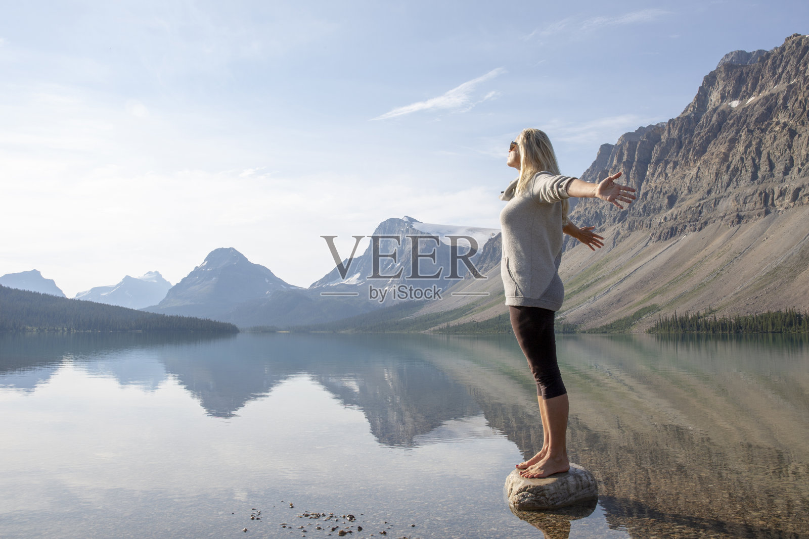 女徒步旅行者站在湖浅的岩石上照片摄影图片