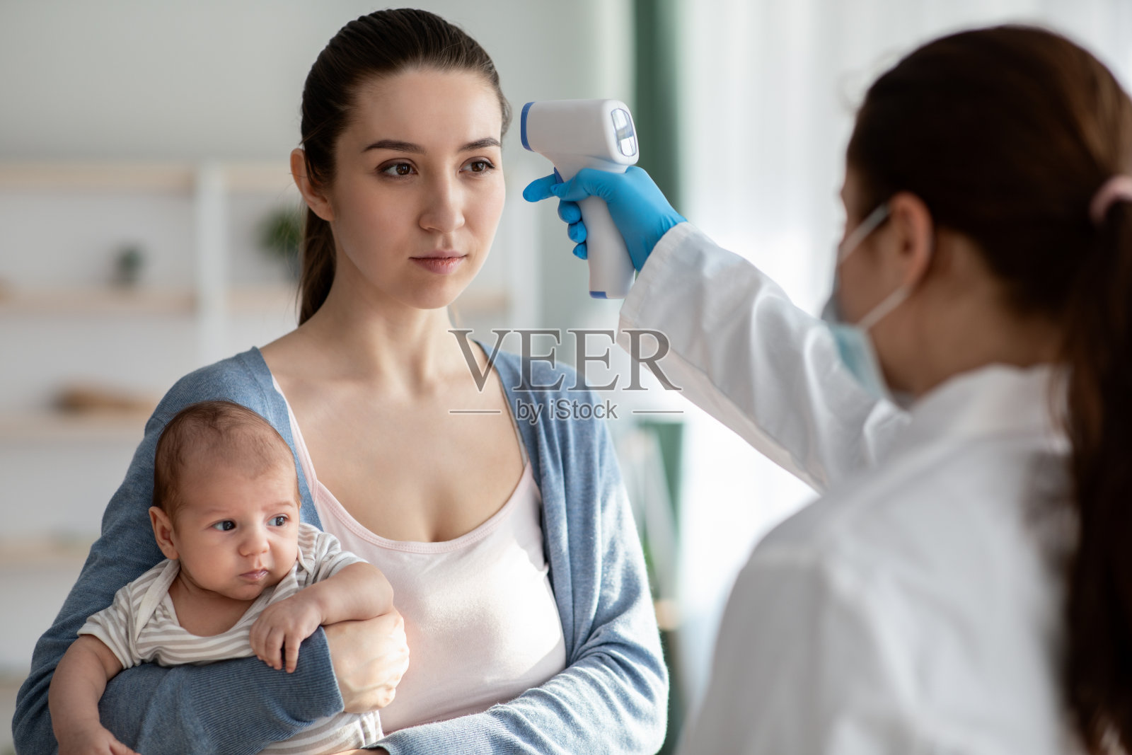医生用红外温度计检查年轻妇女和新生儿的温度照片摄影图片