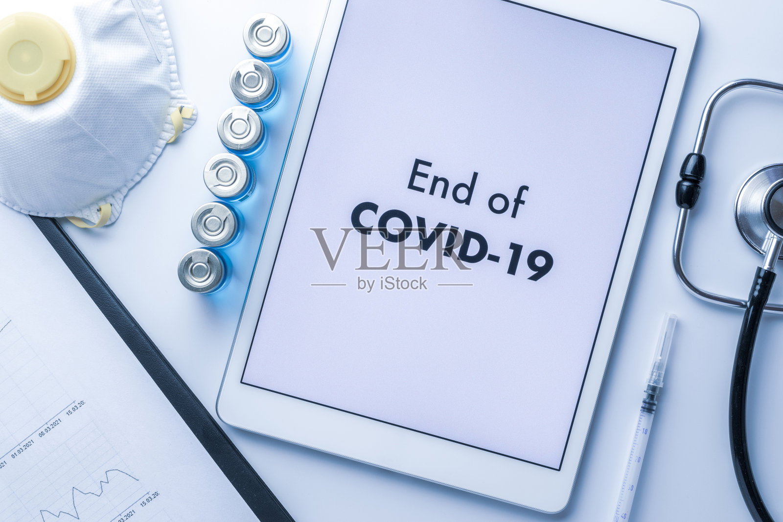 大流行的结束。带针的注射器、医院保健图表、医生听诊器和屏幕上显示医疗设备背景文字的白色平板。2019冠状病毒病概念终结。照片摄影图片