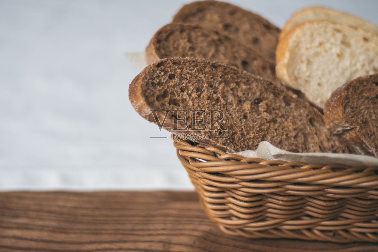 半模糊的柳条篮子，黑色和白色的面包，白色桌布上的木桌照片摄影图片