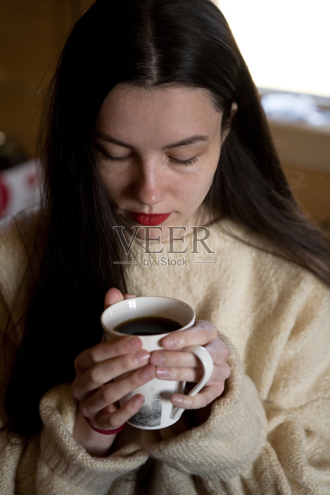 一位穿着毛衣的黑发美人正在喝茶。照片摄影图片