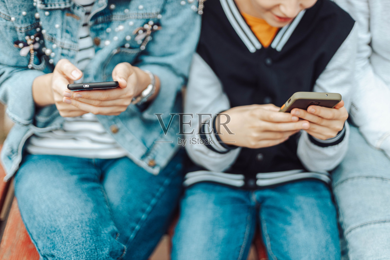 不同年龄层的人坐在街上的长凳上使用智能手机。女人和儿子在休闲牛仔衣服照片摄影图片