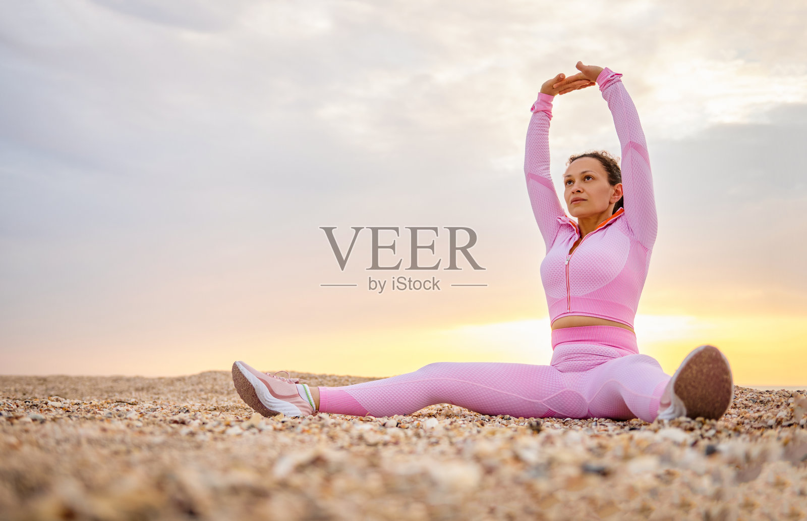 年轻活跃的女士坐在沙滩上，在户外做伸展运动时举起手臂照片摄影图片