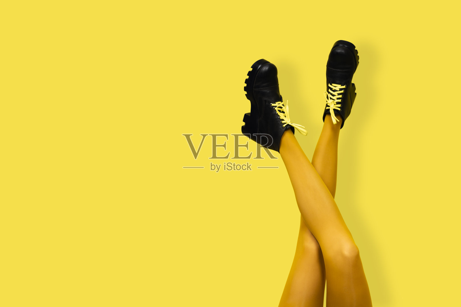 新的灰色女靴在长而细长的交叉女人的腿在明亮的黄色紧身衣孤立在黄色背景。波普艺术概念与沉重的女性靴子。带有复制空间的横幅照片摄影图片