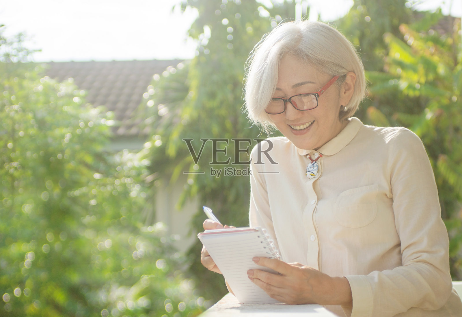 亚洲资深女子站在阳台上，拿着笔记本和笔，思考着。商务，购物清单，支付账单概念，文本空间，拷贝空间照片摄影图片