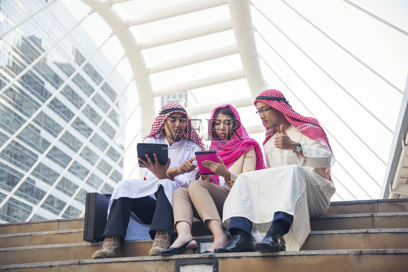 阿拉伯人在阿联酋现代穆斯林城市使用智能平板电脑进行数字营销，触屏讨论。亚洲企业家在户外与老板微笑交谈照片摄影图片