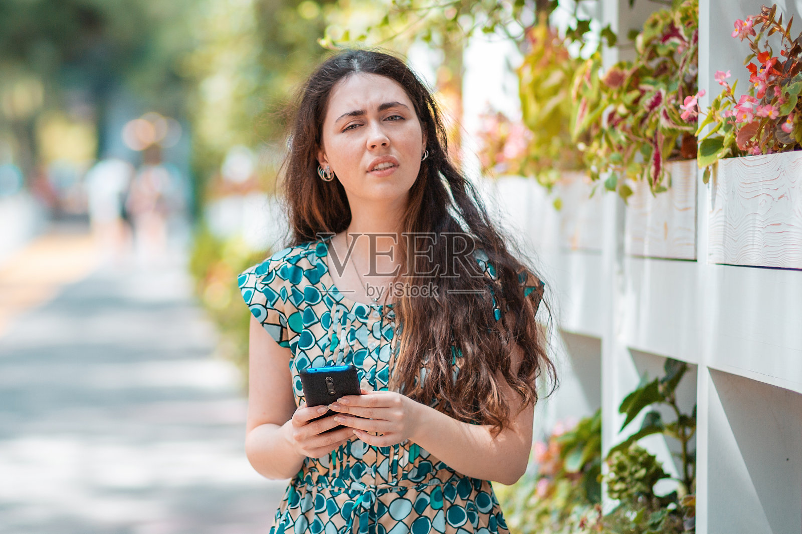 一名一脸愤怒的妇女手里拿着一部智能手机。背景是公园街。沟通和社交网络的概念照片摄影图片