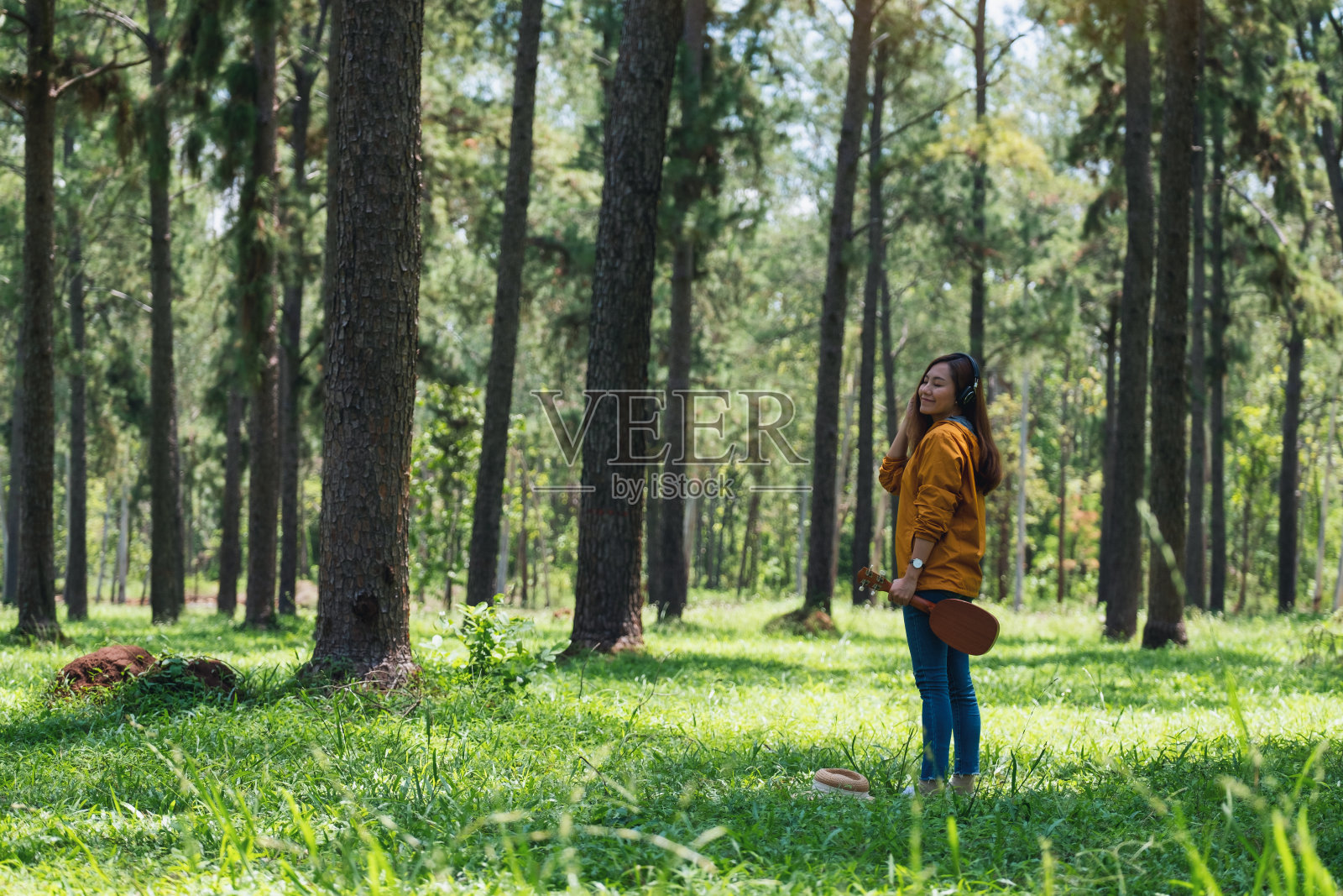 一个女人拿着四弦琴，戴着耳机在公园里听音乐照片摄影图片