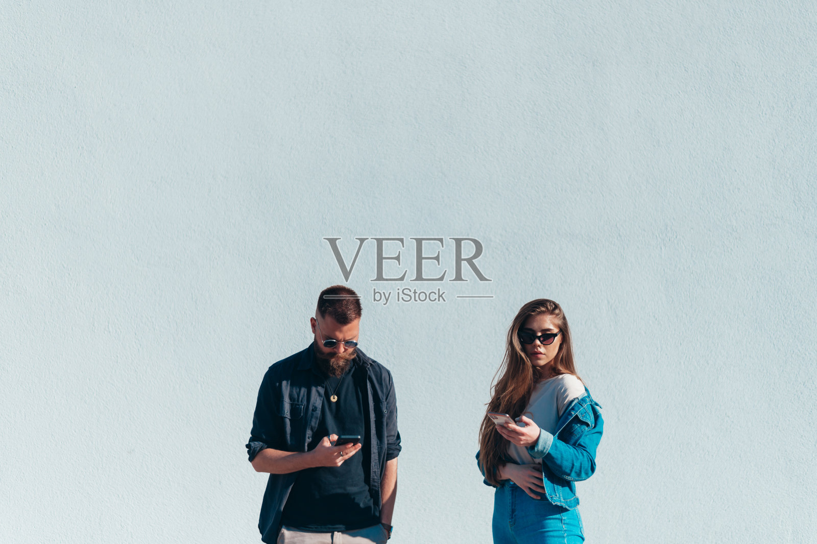 一对情侣在一堵白墙前使用智能手机照片摄影图片