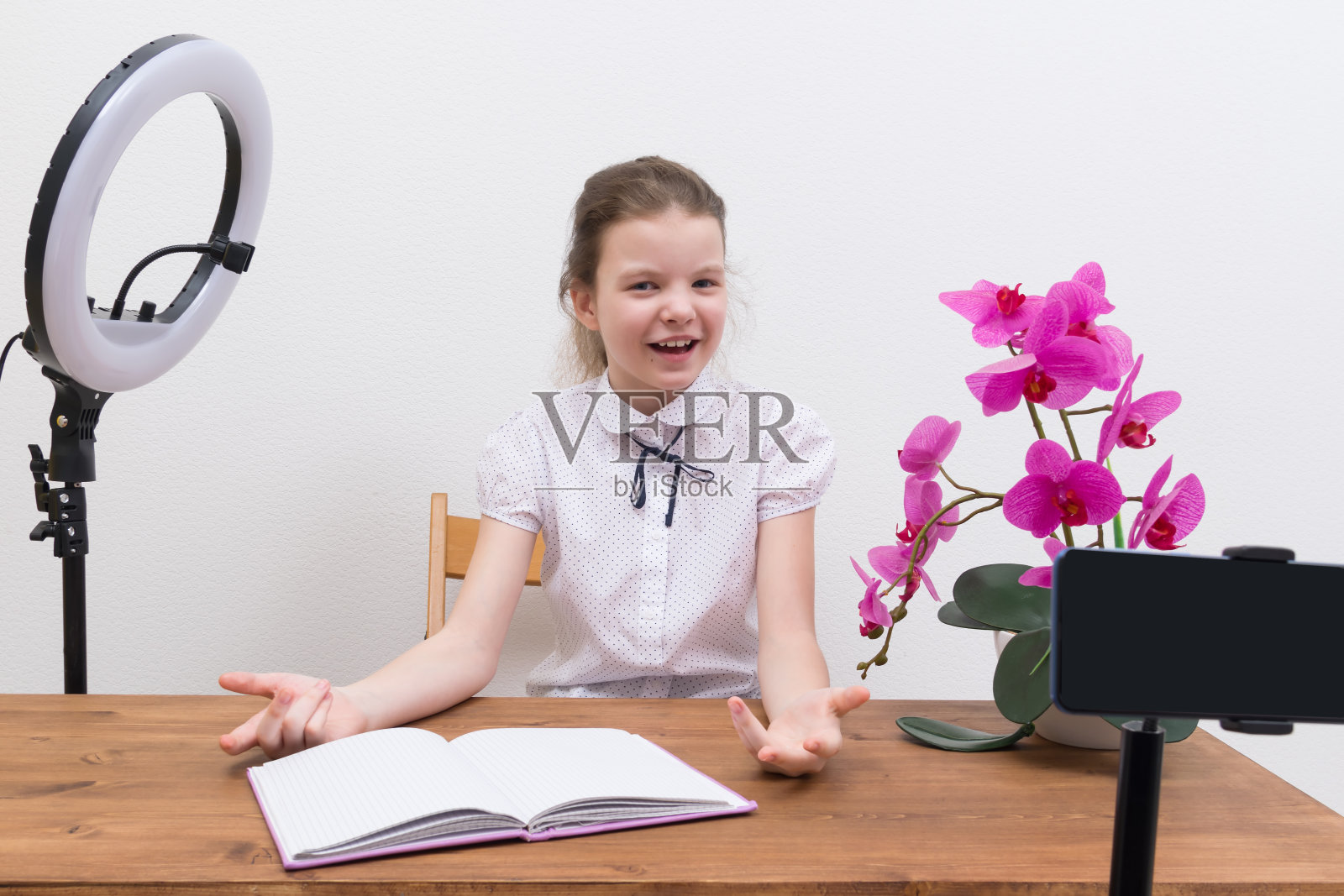 一个开朗的博主女孩被视频拍摄设备、环形灯和智能手机支架包围着，正在为直播做准备照片摄影图片