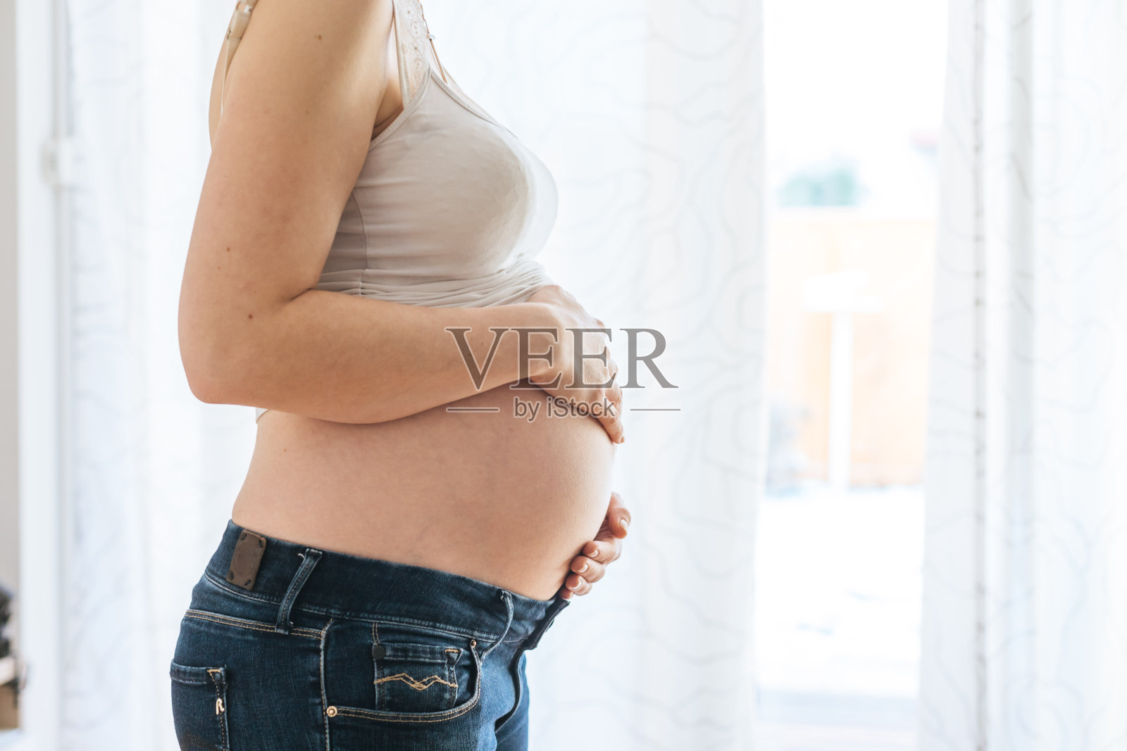 穿着蓝色牛仔裤的快乐孕妇抱着她的肚子，靠近照片摄影图片