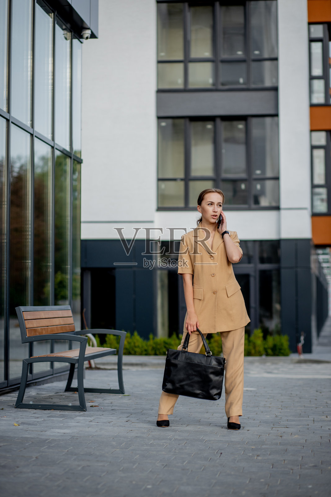 年轻的女主管站在办公楼外面打电话。一个高加索女商人站在公司办公楼对面打电话照片摄影图片