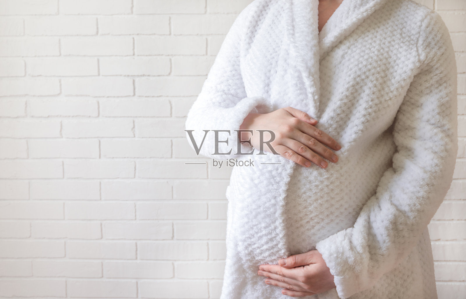 穿着浴袍的怀孕女孩用手抚摸着自己的肚子照片摄影图片