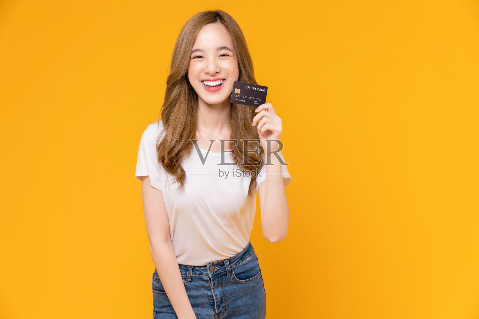开朗美丽的亚洲女人在白色t恤和持有模型信用卡在黄色的背景。照片摄影图片