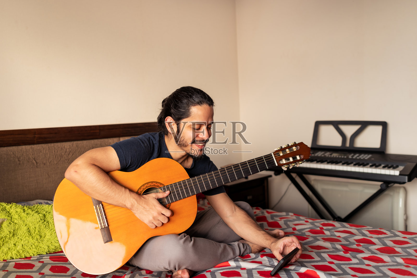 年轻的拉丁男子在家里的卧室里弹吉他照片摄影图片