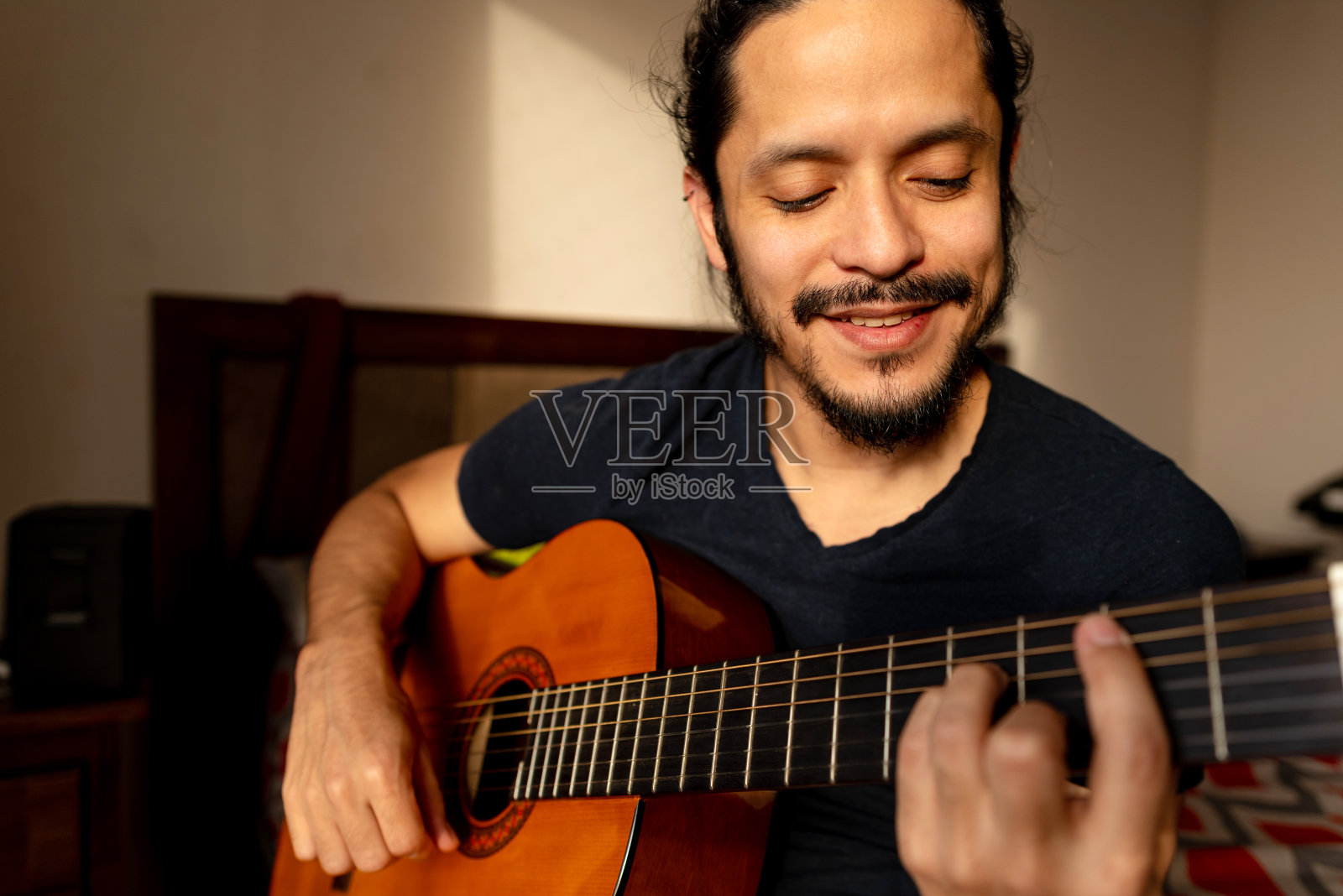 年轻的拉丁男子在家里的卧室里弹吉他照片摄影图片