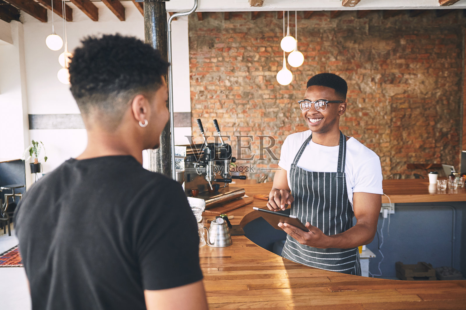 这是一名年轻男子在咖啡馆为顾客服务时使用数码平板电脑的照片照片摄影图片