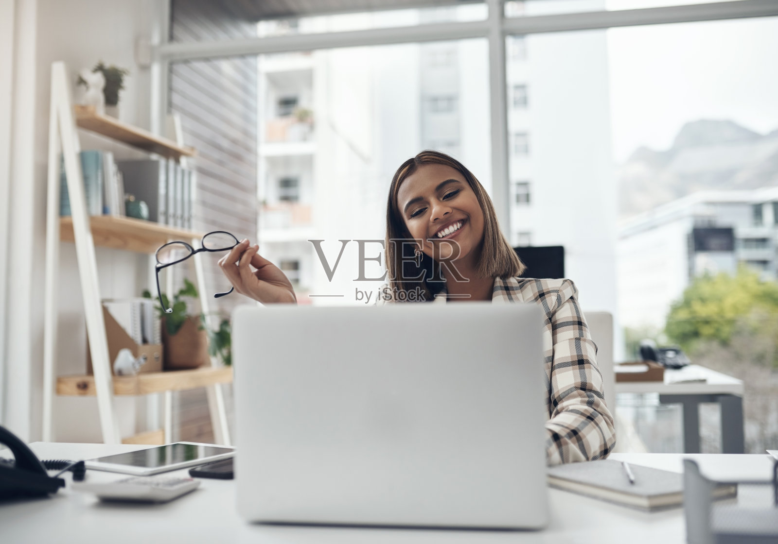 照片中，一位迷人的年轻女商人独自坐在办公室里，使用着她的笔记本电脑照片摄影图片