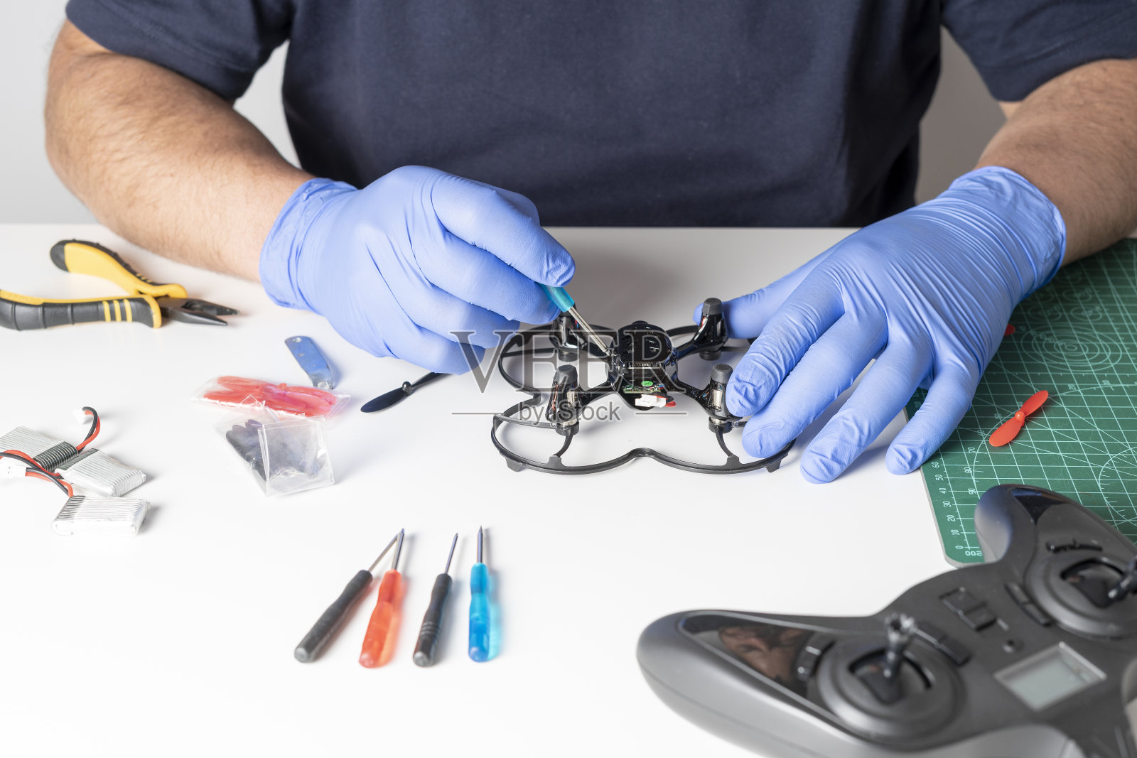 用螺丝刀拆卸玩具无人机的人。各种工具和无人机的备件放在一张桌子上。手的修复照片摄影图片