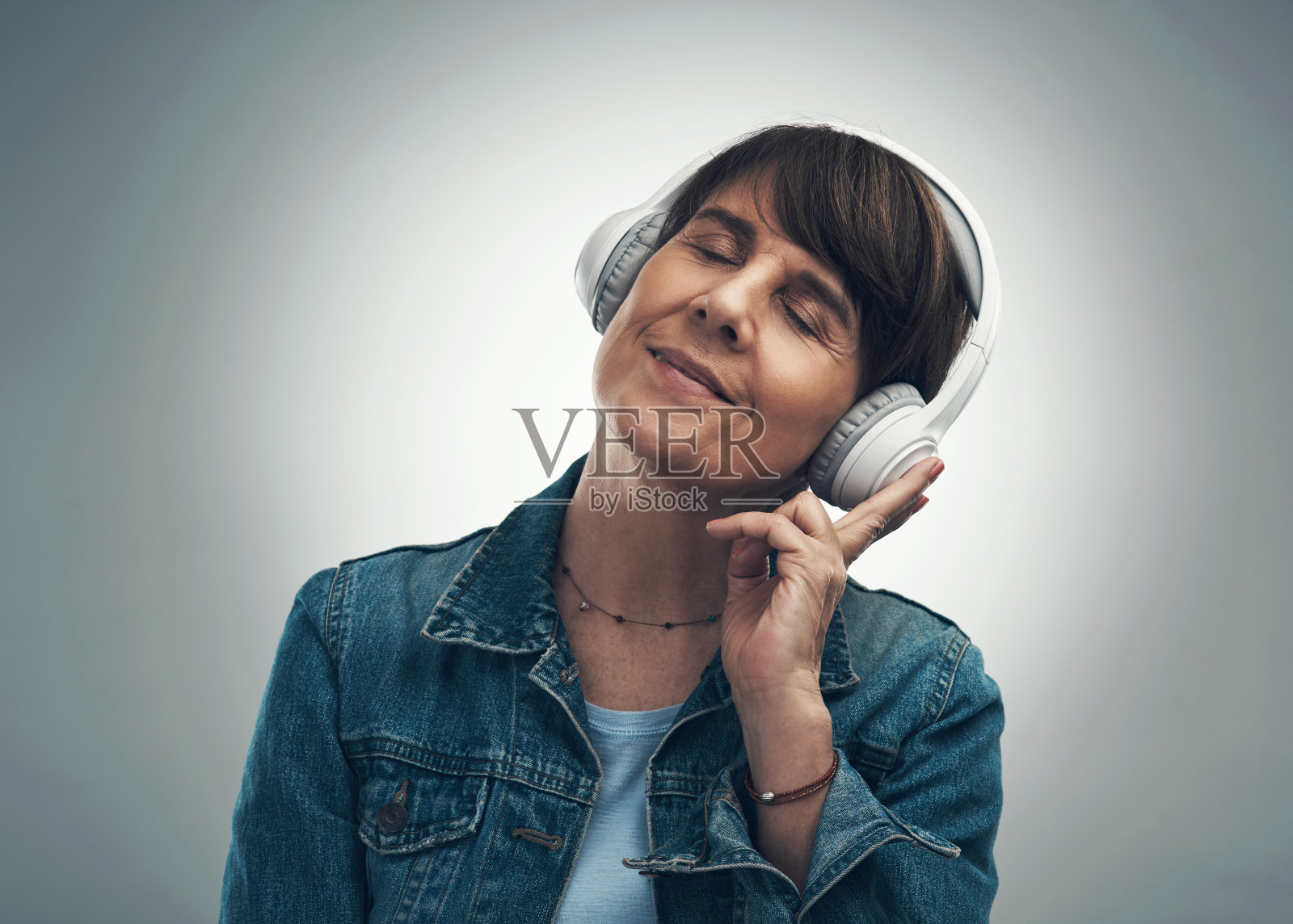 一名戴着耳机的年长女性在灰色背景下的照片照片摄影图片