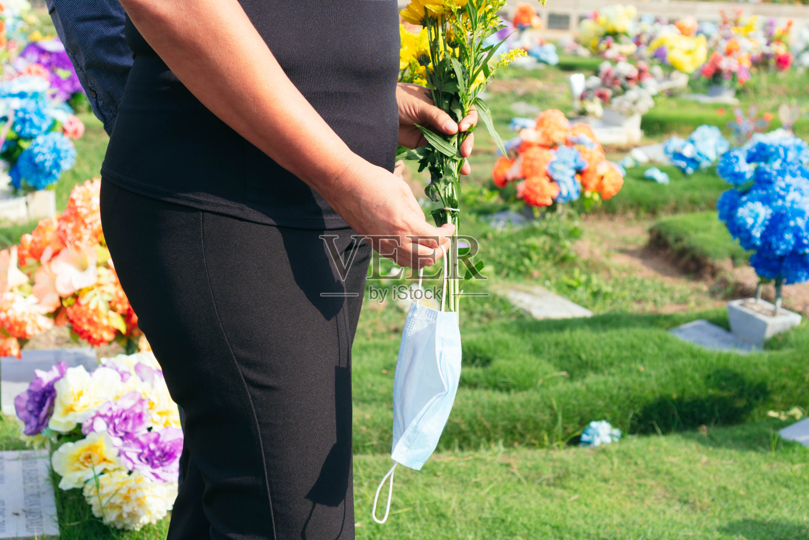 一对戴着医用面具的悲伤夫妇在墓地里。照片摄影图片