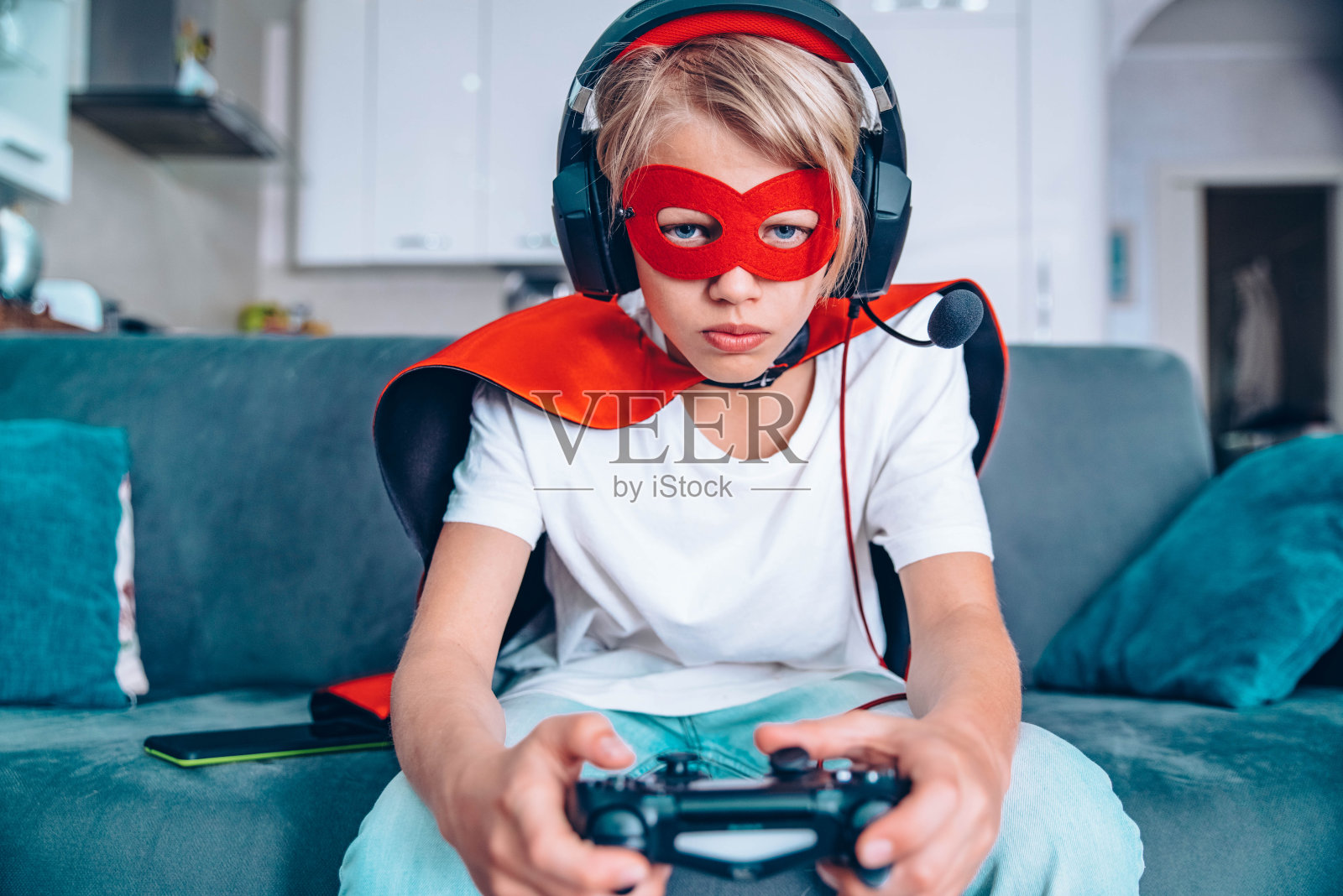 超级英雄的孩子坐在家里的沙发上玩电子游戏-孩子，游戏和科技概念照片摄影图片