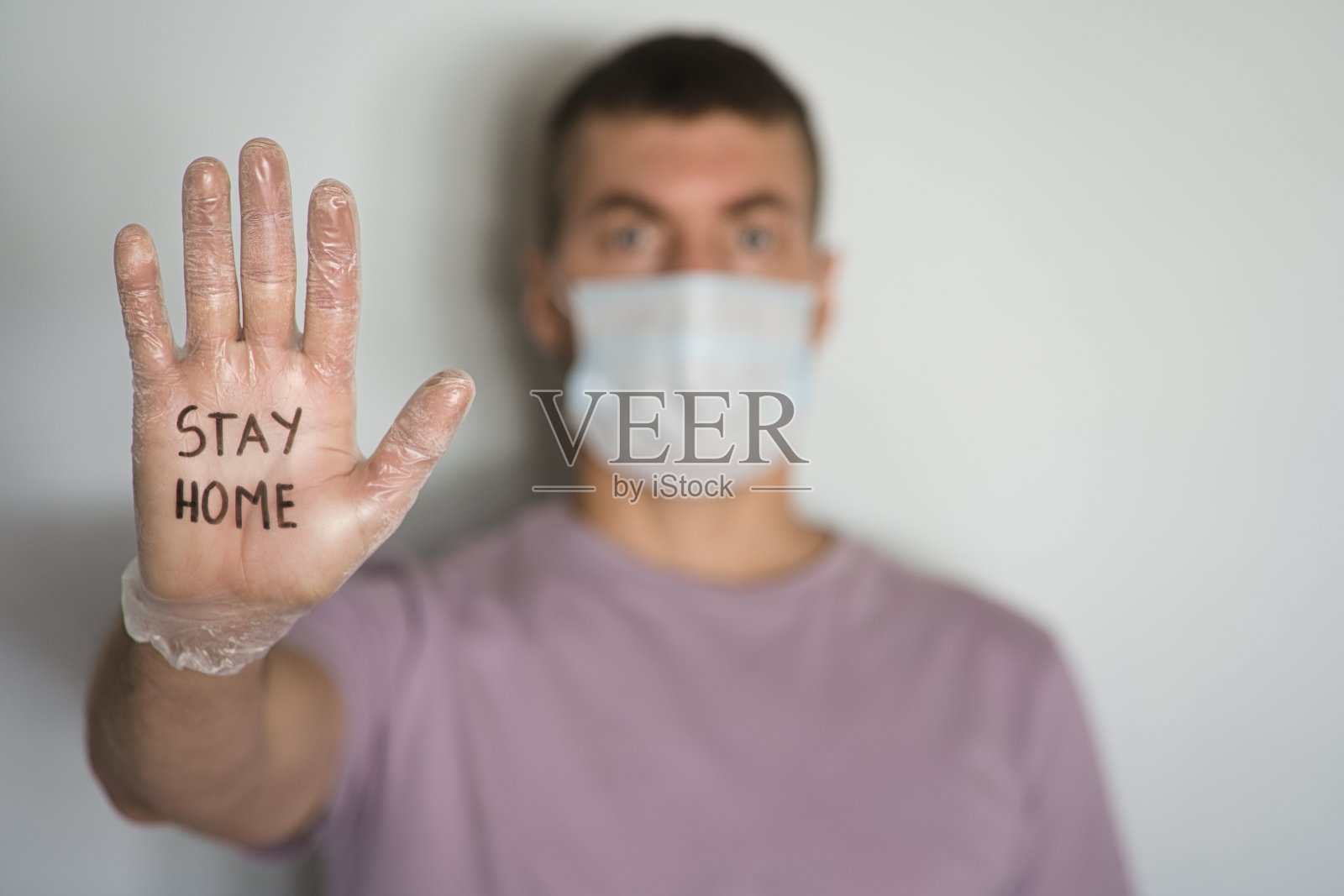 年轻的白人男子戴着写着"待在家里"的口罩和卫生手套。照片摄影图片